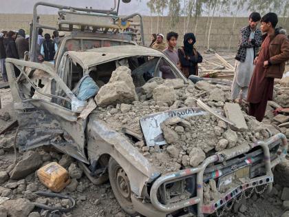 Local residents stand next to a damaged car at the site of a cross-border Pakistani army strike in the Behsud district of Nangarhar province, Afghanistan.