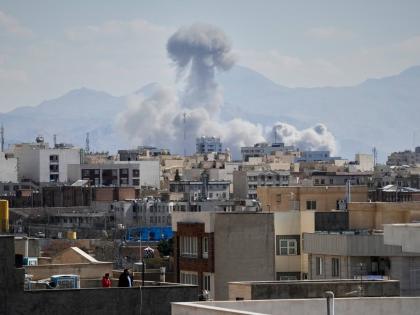People watches from a rooftop as a plume of smoke rises after a strike in Tehran.