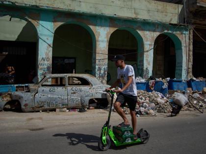 A man rides a scooter past a wrecked car and garbage during a blackout in Havana.