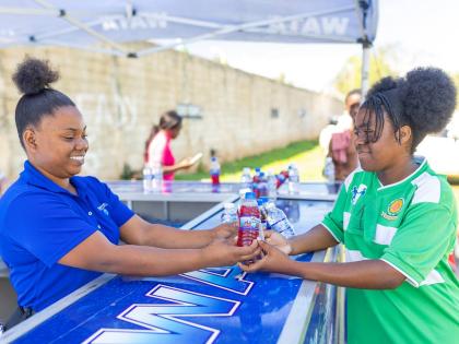 Savana Clarke (left), WATA brand representative, hands a chilled bottle of water to Rushawna Ebanks at the hydration station during WATA’s Hydrate to Educate School Tour stop at BB Coke High School in St Elizabeth on Wednesday, March 5. The visit formed 