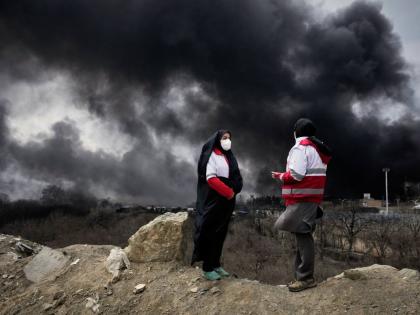 Two women from the Iranian Red Crescent Society stand as a thick plume of smoke from a US-Israeli strike on an oil storage facility rises in the sky in Tehran.