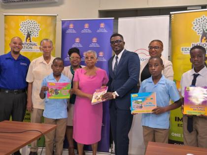 Carlong Publishers chair, Shirley Carby (centre), presents Fitzroy Abbott, principal of Christiana Moravian Primary and Infant School in Manchester, with a copy of one of the textbooks donated by the company. Joining them are (from left) Carlong Publishers