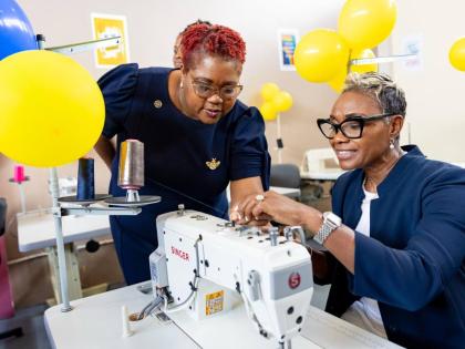 State Minister in the ministry of National Security and Peace, Juliet Cuthbert-Flynn (right), is being assisted by Chief Technical Director in the ministry, Shauna Trowers, with threading a sewing machine in the new sewing lab at the South Camp Juvenile Co