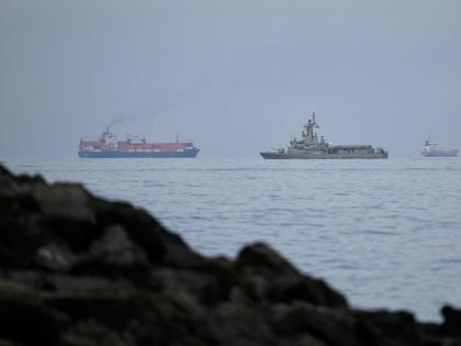 A UAE navy ship sails next to a cargo ship in the Strait of Hormuz as seen from Khor Fakkan, United Arab Emirates.