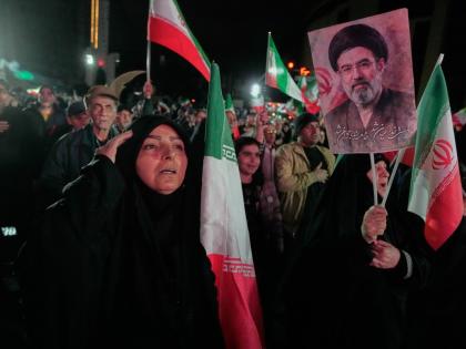 A woman salutes while singing the national anthem as another holds a picture of Iranian Supreme Leader Ayatollah Mojtaba Khamenei during a pro-government gathering in a square in western Tehran, Iran on March 25, 2026. (AP Photo/Vahid Salemi)