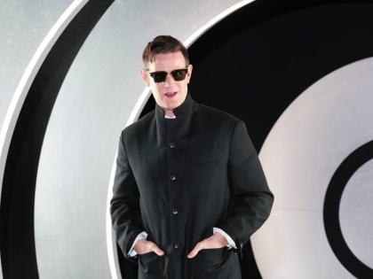 Matt Smith wears a polished, dark, tailored suit. 