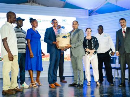 Keneil Gray (fourth left), supported by fellow project beneficiaries, presents Floyd Green (fourth right), minister of agriculture, fisheries and mining, with a produce basket in the presence of Dr Ana Touza (third right), FAO representative for Jamaica, T