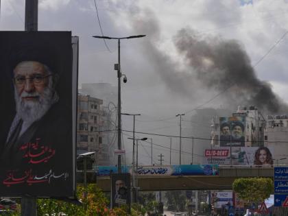 A portrait of Iran's late Supreme Leader Ayatollah Ali Khamenei, left, is seen, as smoke rises following an Israeli airstrike in Dahiyeh, Beirut's southern suburbs, Lebanon on March 30, 2026. (AP Photo/Hassan Ammar)