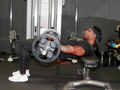 Brown demonstrates the hip thrust exercise, with shoulders on a bench and weight placed on the hips, lifting the hips upward in a controlled motion.