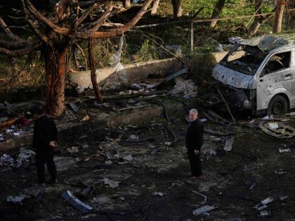 People stand near a damaged van beside scattered debris following an Israeli strike in Beirut, Lebanon.