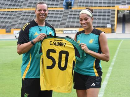 Hubert Busby (left), head coach of the Reggae Girlz, presents defender Chantelle Swaby with a jersey ahead of her 50th game for the national team. 