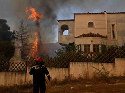 A volunteer firefighter observs a flame rising next to a house during a wildfire near Porto Germeno, northwest of Athens, Greece, Sunday.
