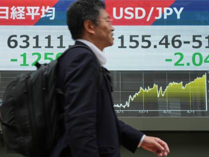 AP 
A man walks past an electronic board showing Japan’s Nikkei index, and US dollar-Japanese yen exchange rate at a securities firm in Tokyo on Monday, August 3.  