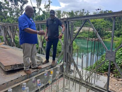 Works Minister Robert Morgan (right) and Wayne Cover, the National Works Agency’s parish manager for St James, survey a section of the Over River community bridge in St James on Wednesday.