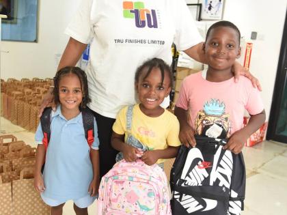 Sharon Harris, managing  director, Tru Finishes Limited, presents schoolbags to children from the Maxfield Avenue area during the company’s annual back-to-school treat for children in the area recently.