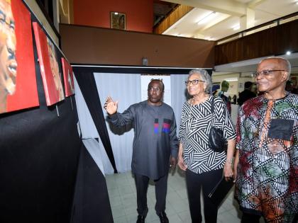 Professor Hopeton Dunn (left) introduces an art piece from his collection to former Governor General Sir Kenneth Hall (right) and his wife Rheima Hall at the opening of the ‘Kgotla!’ African Art and Artifact Exhibition at the Main Library of The Univer