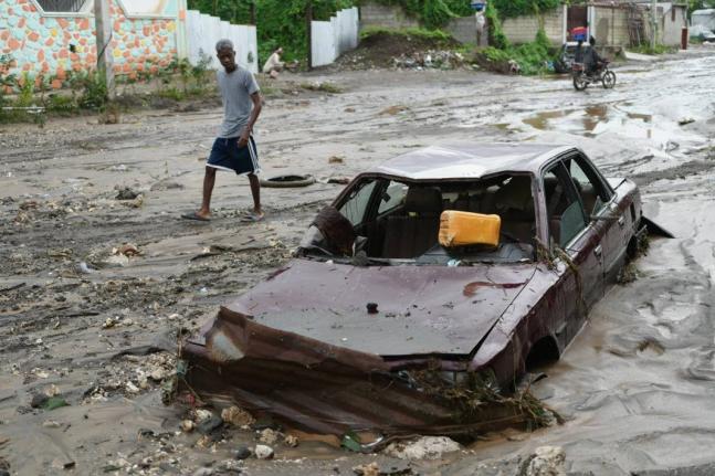 A pedestrian looks at a flooded car in the aftermath of Hurricane Melissa in Petit-Goave, Haiti, Thursday, October, 2025. 