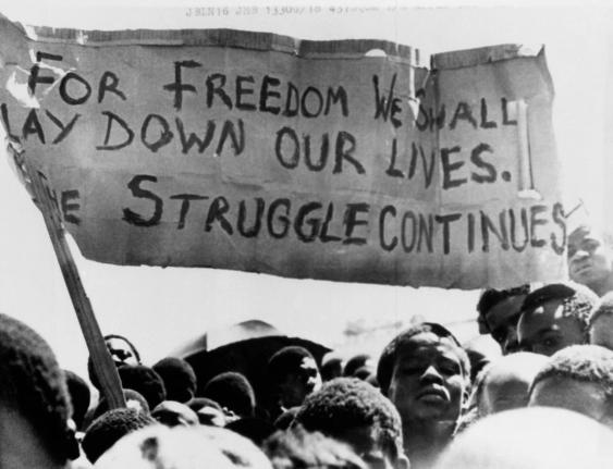 A banner is held aloft above black students in Johannesburg, South Africa, in the township of Soweto where they rallied after the funeral of a 16-year-old black student who died in jail on October 18, 1976. 
