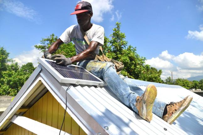 Demar Banton a carpenter working with Food For The Poor installs a solar panel on the roof of a newly bult house for a family in Kingston.
