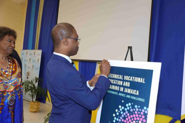 Dr Kevin Brown, president of the University of Technology, Jamaica and chairman of UTech Press, signs a replica of the cover of Technical Vocational Education and Training in Jamaica: Achievements, Impact, and Challenges, launched on November 26.
