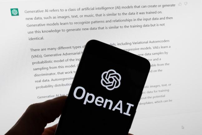 The OpenAI logo is displayed on a mobile phone in front of a computer screen with output from ChatGPT, March 21, 2023, in Boston. (AP Photo/Michael Dwyer, File)