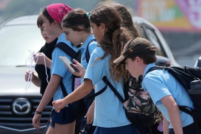 A school girl uses her phone as she walks with a group of kids in Sydney.