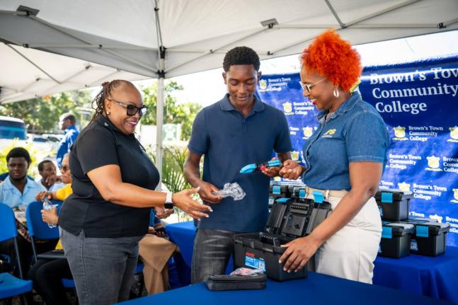 JPS Foundation Head Sophia Lewis (right) and Brown’s Town Community College Claudeth Haughton look on as Electrical Installation Level II student Rajaunie White unpacks items in his electrical toolkit donated by the foundation.