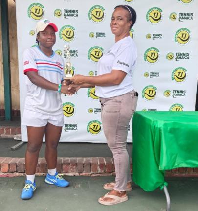 Jade Fearon (left) collects one of her trophies from Ann Marie Maxwell, All Jamaica Tennis administrator,  during the All Jamaica Tennis Championship held at the Eric Bell National Centre on Saturday, December 20, 2025. Fearon won the under-16 and under-18