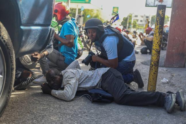 Journalists take cover from the exchange of gunfire between gangs and police in Port-au-Prince, Haiti.