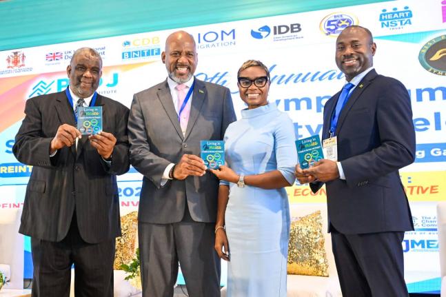 Minister of State in the Ministry of National Security and Peace, Juliet Cuthbert-Flynn, is presented with a copy of the ‘Living in Jamaica: A Guide to Services and Support’ handbook by Director General of the Planning Institute of Jamaica (PIOJ), 