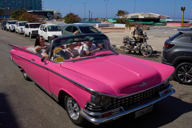 
Tourists travel in a classic American car next to a line of drivers waiting to buy fuel for their cars in Havana, Cuba.
