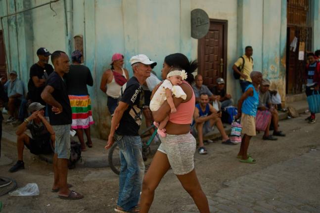 A woman walks with a baby in her arms past people lined up to buy bread during a blackout in Havana, Cuba,