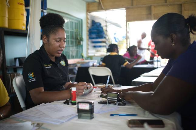 A representative from the Tax Administration Jamaica (TAJ) assists a resident of Savanna-la-Mar with documentation at the Project STAR Civil Documentation Community Hub, hosted at the New Market Oval Community Centre.