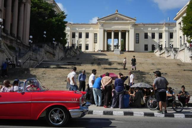 A car rides past students sitting outside the University of Havana during a protest over an energy crisis that has disrupted classes in Havana, Cuba, Monday, March 9, 2026. 
