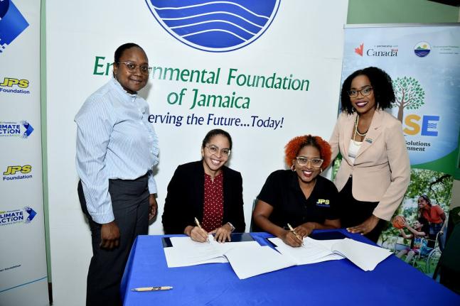 EFJ boss, Nicole Adamson (seated left) and JPS Foundation Head, Sophia Lewis (seated right) sign the MOU while Joni Jackson (left), project manager for the J-USE project, and Audrey Williams, media and public relations manager at JPS, witness the signing.