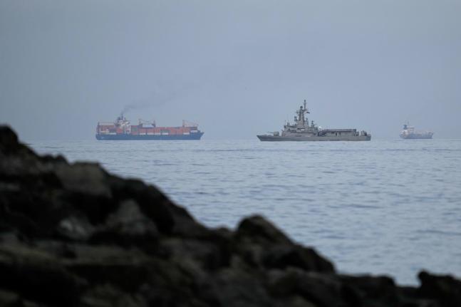 A UAE navy ship sails next to a cargo ship in the Strait of Hormuz as seen from Khor Fakkan, United Arab Emirates.