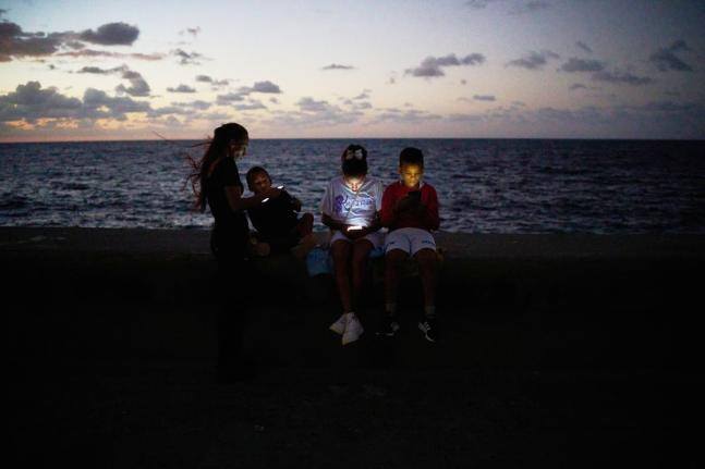 Children look at their phones while sitting on the Malecón wall during a blackout in Havana, Cuba.