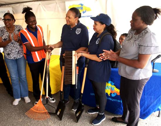President of the Majesty Gardens Community Development Corporation, Jaheim Mitchell (second left), receives cleaning tools from Pan American Development Foundation Project Coordinator, Kimberly Seymour-Brown, at the Community Clean-up, E-Waste Drive, and t