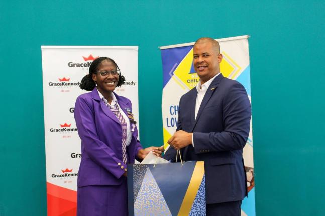 GraceKennedy Group CEO Frank James presents a laptop to Aldi-Anna Lewis, sixth form student at deCarteret College, and the 2025 Top Performer in the National Child Month Committee’s (NCMC) Youth Academic Achievement Awards. The presentation took place du
