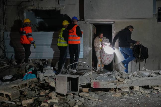 Residents carry personal belongings as they leave a building damaged in a missile strike in Tel Aviv, Israel on March 28, 2026. (AP Photo/Maya Levin)