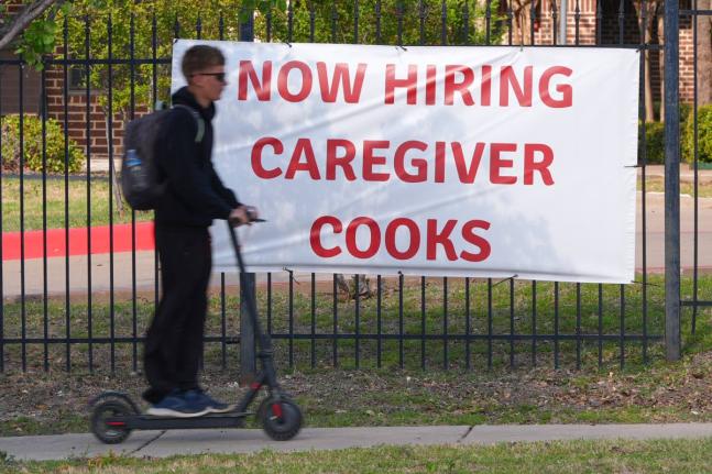 AP 
A ‘now hiring’ sign sits by the sidewalk as a rider on a scooter passes in Garland, Texas, Monday, March 23. 