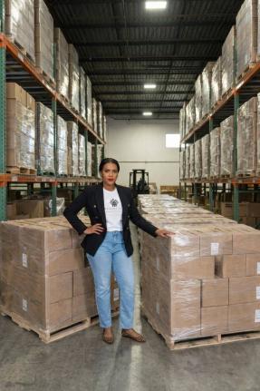 Kith‑Ann Excell, organiser of the Comfort and Care Relief Drive, stands alongside donated relief supplies at a Florida warehouse.