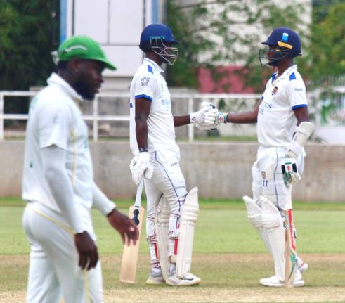 Barbados Pride batsmen Kevin Wickham (centre) and Kraigg Brathwaite meet mid-pitch during their century stand against the Jamaica Scorpions on day three of their West Indies Championship match at Sabina Park yesterday. Jamaica Scorpions’ Kirk McKenzie is