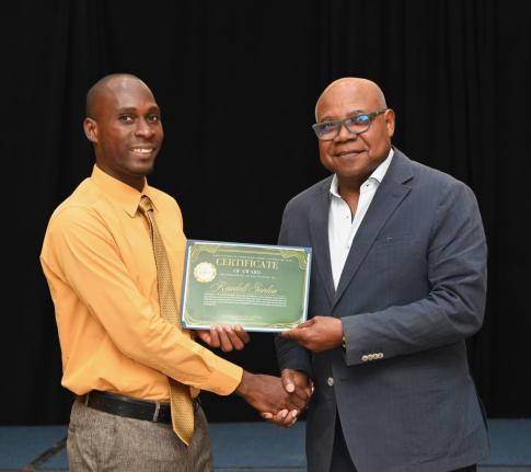 Randell Gordon (left), a recent beneficiary of the East Central St James Scholarship and Welfare Fund, receives his presentation certificate from Edmund Bartlett, minister of tourism and member of parliament for St James East Central, during the 30th annua