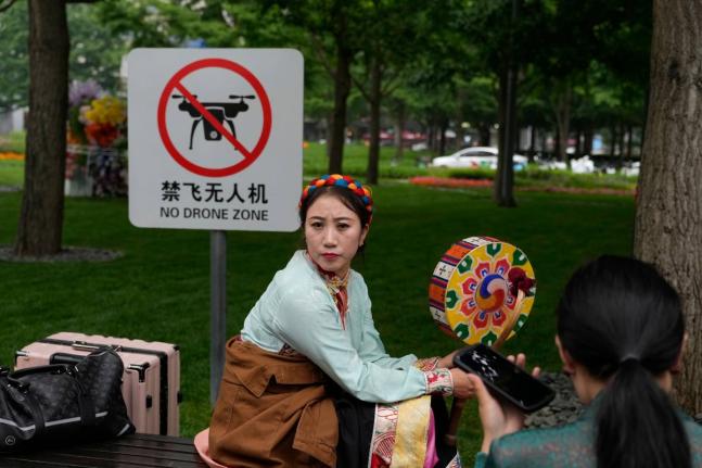 A performer rests near a “No Drone Zone” sign in Beijing, on May 31, 2023. 