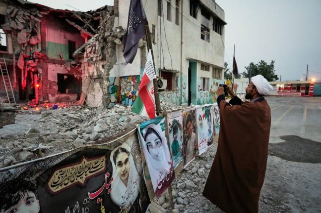 A cleric takes a photograph at the shattered Shajareh Tayyebeh school, which has become a place of mourning and a memorial to those killed in a US airstrike on February 28, in Minab, southern Iran, September 7.