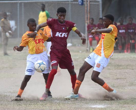 Garfield Massop (centre) of Denham Town High attempts to force his way between Joseph Ward (left) and Kwasi Clarke  of Donald Quarrie High during their Manning Cup football match at Tivoli High School yesterday.