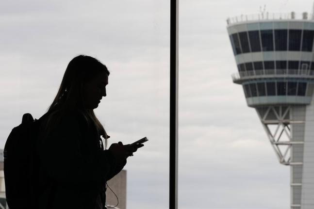 FILE - A traveler with a smartphone walks past an air traffic control tower at Philadelphia International Airport in Philadelphia on March 27, 2026. (AP Photo/Matt Rourke, File)
