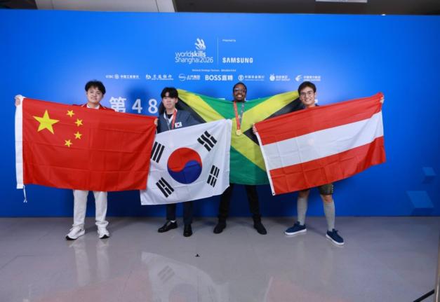 Jamaica’s WorldSkills Shanghai 2026 Optoelectronic Technology gold medallist, Brandon Brown (second right), proudly displays the national flag at the Winners’ Circle, during Sunday’s closing ceremony at Shanghai World Expo Cultural Center. He is join