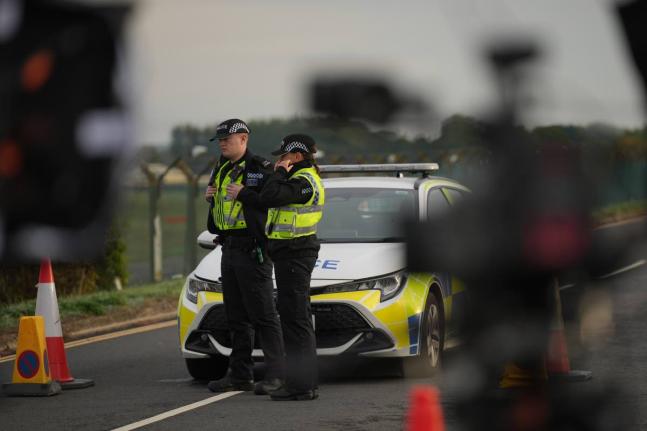 Police officers guard a road leading to RAF Fairford, after an incident in Fairford, England, Monday.